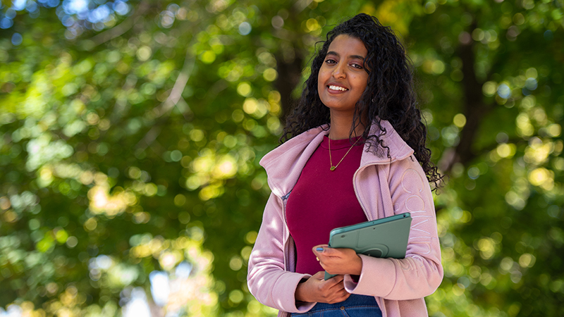 Student with iPad smiling outside