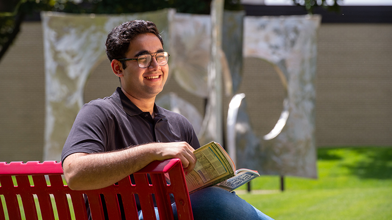 Young man sitting on red bench with book in hand, smiling off into the distance