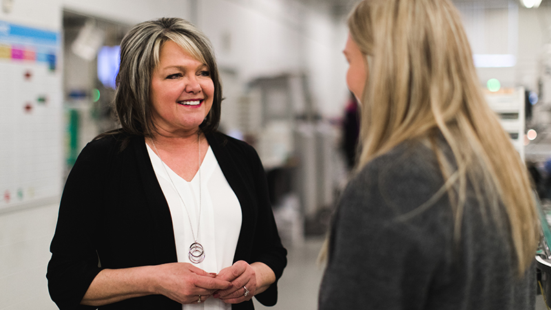 Two nicely dressed women speaking to one another at work place