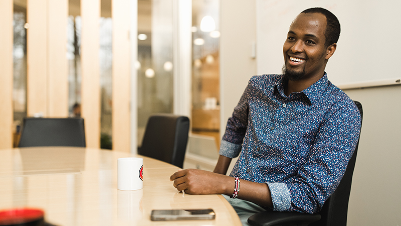 An older male student leans back and smiles in a meeting room