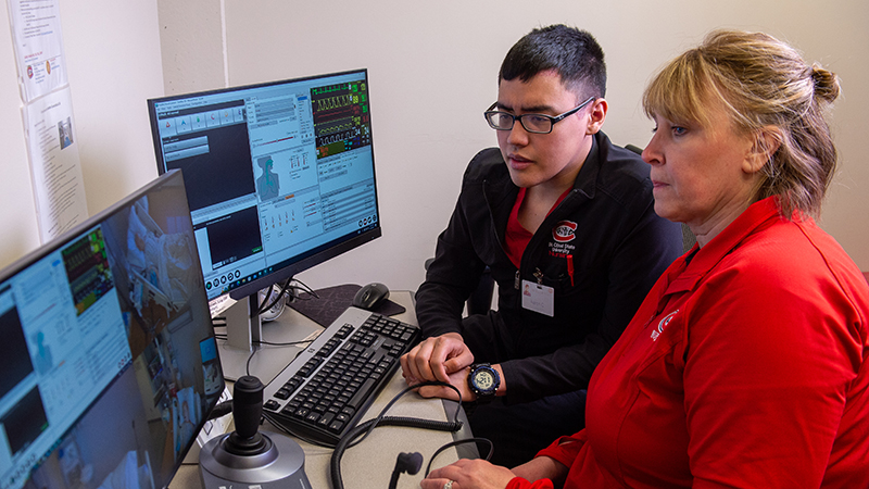 A nursing instructor shows a student something in an observation room