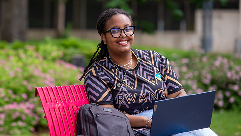 SCSU student sitting on red bench with laptop