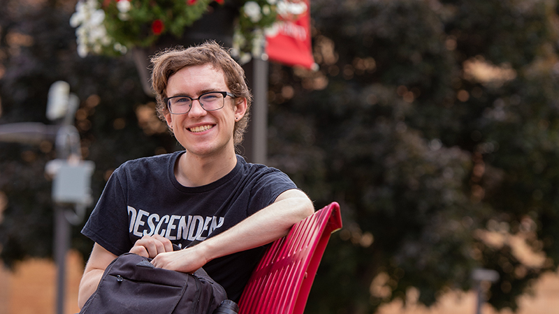A SCSU student smiles for a photo on a campus bench