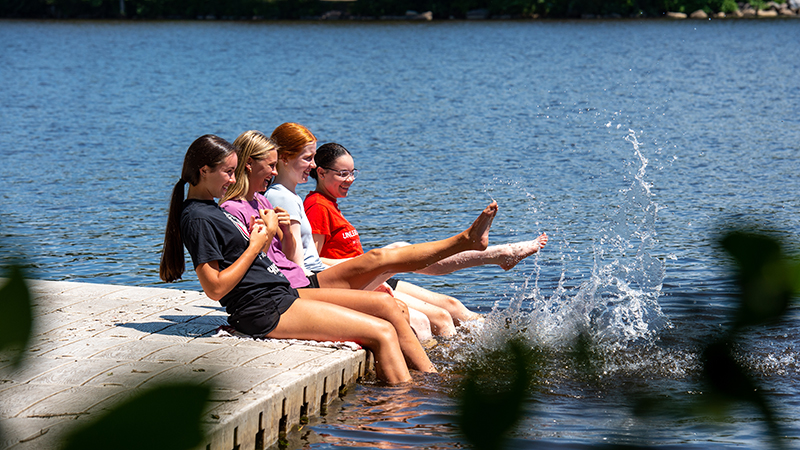 A group of SCSU students sitting on dock and splashing feet in the Mississippi River