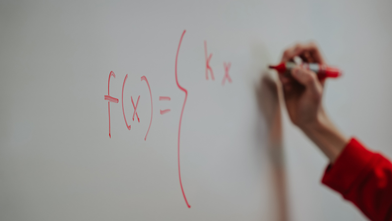 A close up of hand writing out a math problem on a white board