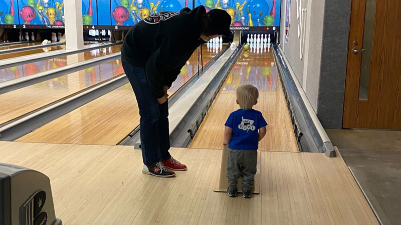 A toddler and an adult look down a bowling lane with stacked bowling pins at the Underground located in Atwood Memorial Center