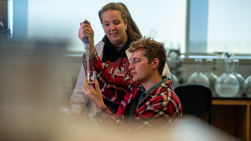 Pair of college students adding liquid to glass tub