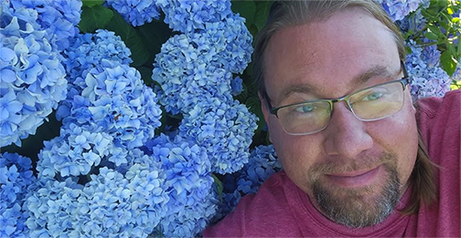 Dr. Cook stands next to blue flowers in full bloom outside