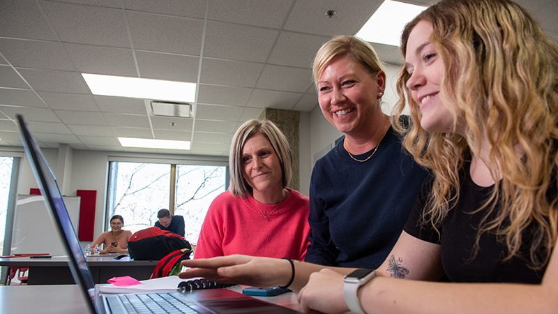 Two advisors help a student register on their laptop
