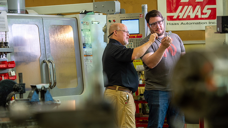 An engineering professor looks at small mechanical parts with a student