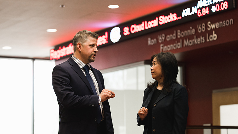 Two professionally dressed people stand outside of the Financial Markets Lab at St. Cloud State University
