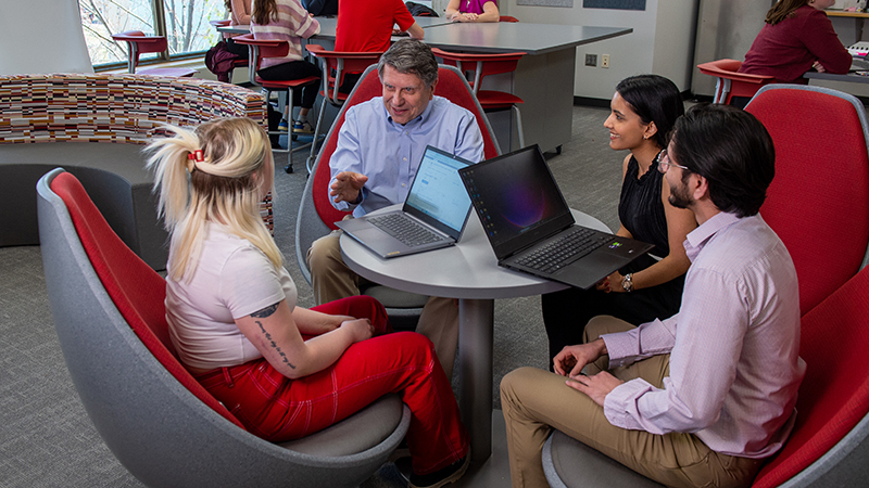 Three business students gather in a lounge with professor