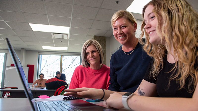 A student receives help on laptop from two staff persons