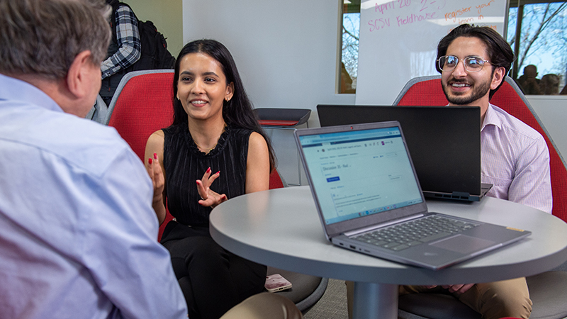 Students speak casually with a professor in a student lounge space