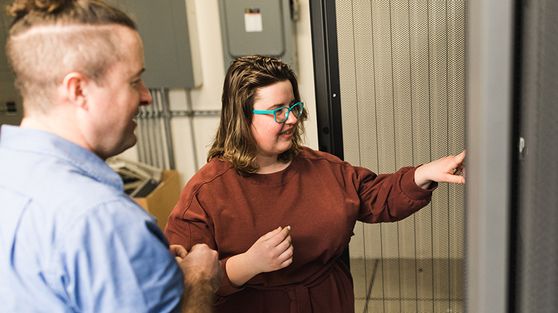 A student examines an IT rack with staff person