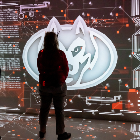 Person standing in front of a large illuminated St. Cloud State University Huskies logo display in an indoor technology space