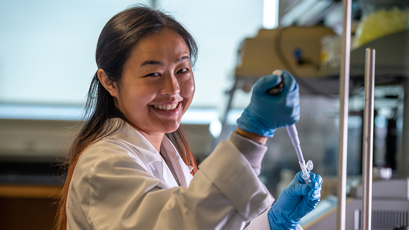 Lab student in white coat smiling at camera