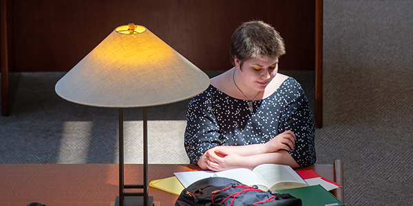 A student studying at a library table, sunlight shining down on face