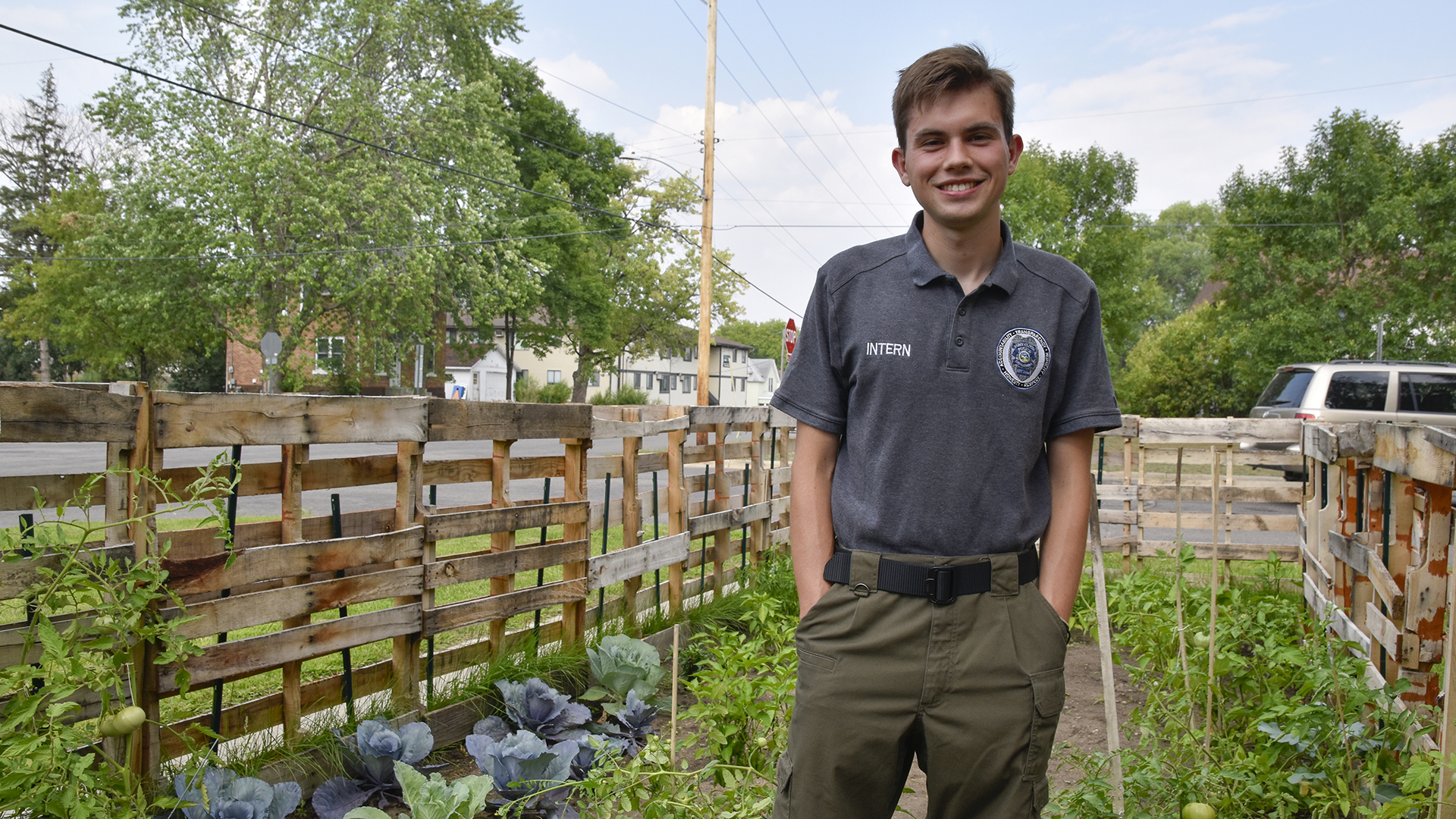 A person stands in the St. Cloud State University community garden on a partly cloudy day with greenery in the background