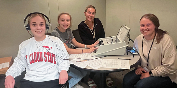 Four students seated at table working with audiology equipment.