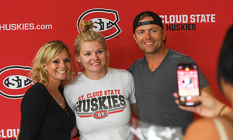A student stands for a photo with two adults in front of a large St. Cloud State Huskies banner