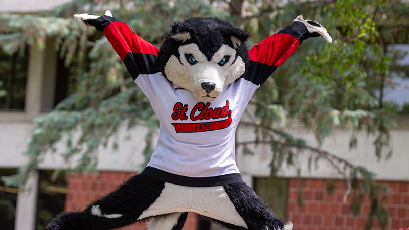 Blizzard, the St. Cloud State University mascot, jumping in front of Centennial Hall
