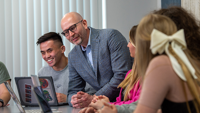 Education students gather around their laptops with a professor