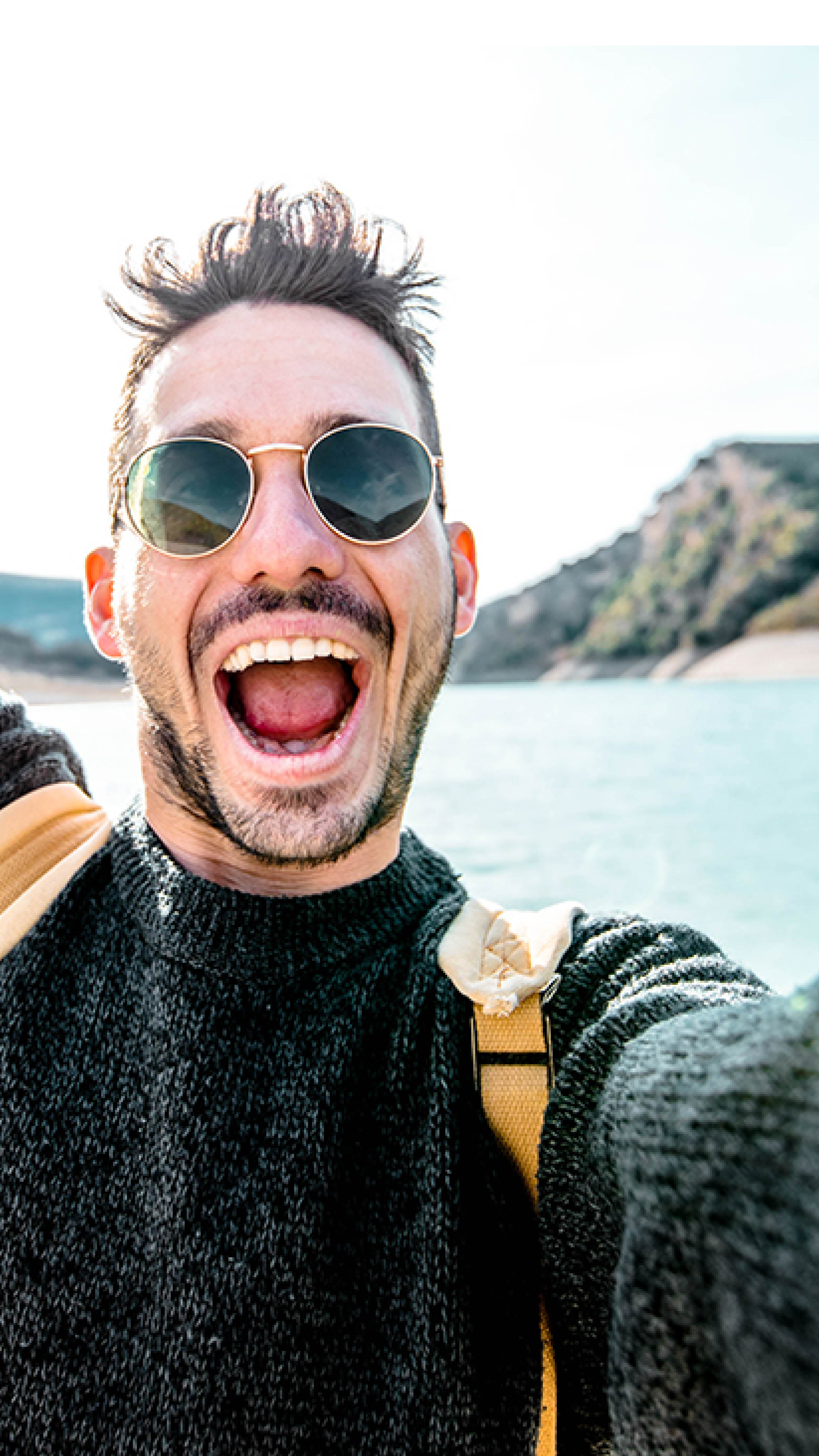 Young man taking an excited selfie in the valley of a mountain range