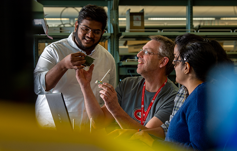 Students reviewing a circuit board with a professor 