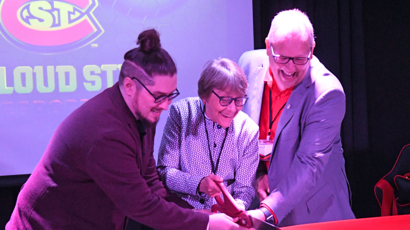 Three people cutting red ribbon with large scissors