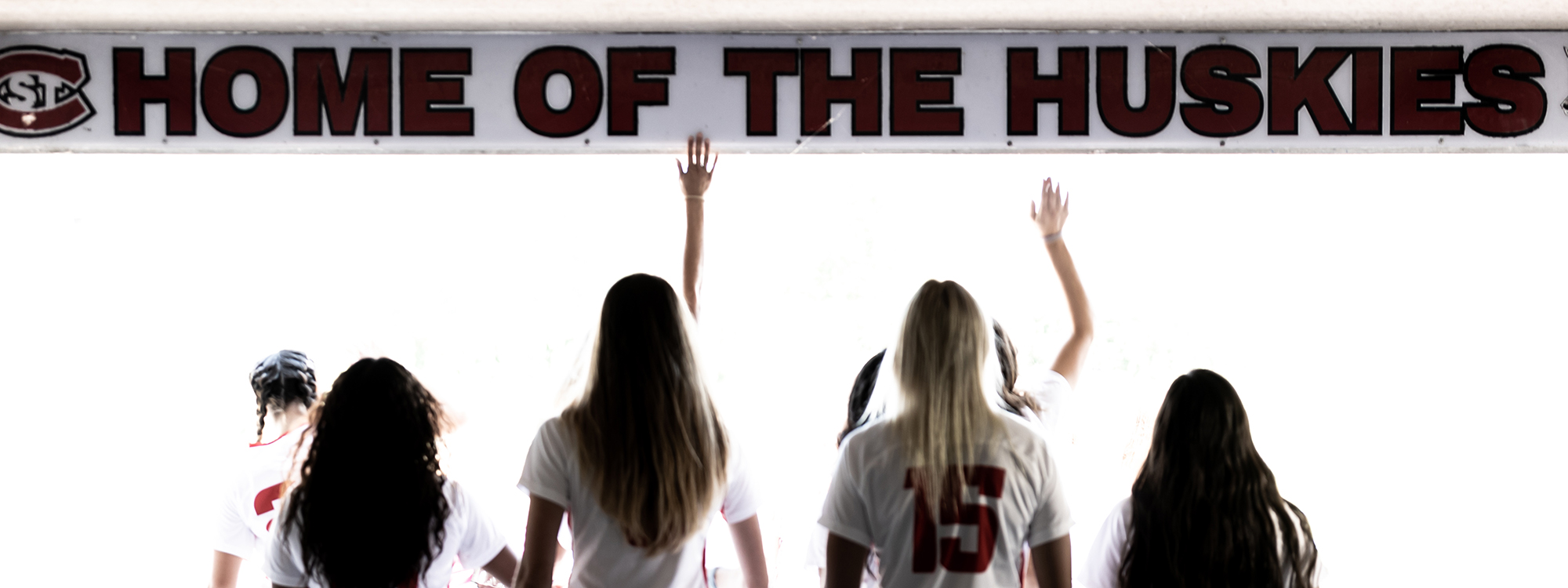 Members of women's soccer team entering stadium with bright daylight in background