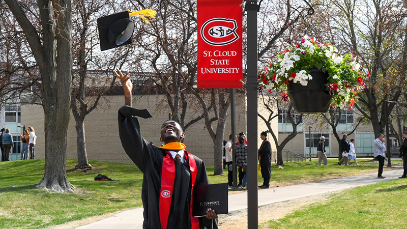 St. Cloud State University graduate throwing cap in the air under a St. Cloud State University banner