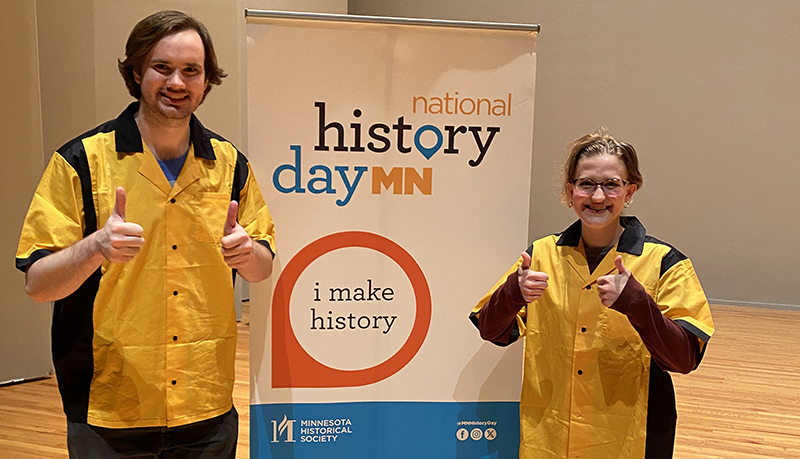 History Day MN interns posing for photo by banner on stage