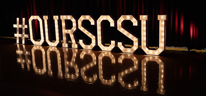 Large light-up letters sit on the ballroom floor spelling out #OurSCSU