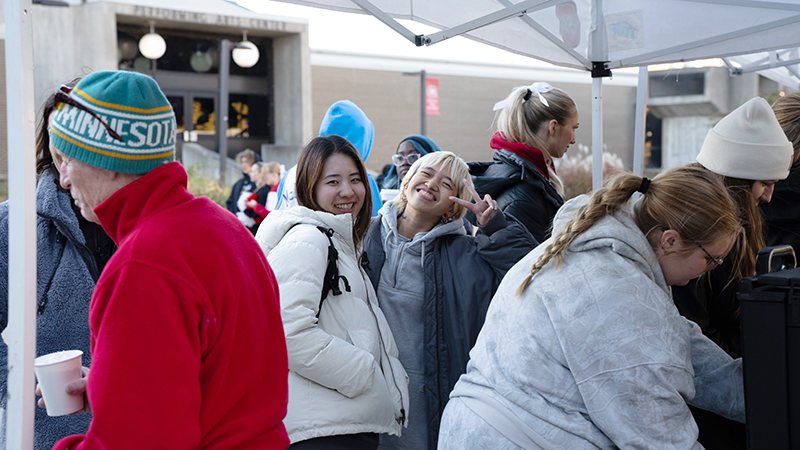 students smile and show peace sign to the camera during campfire event