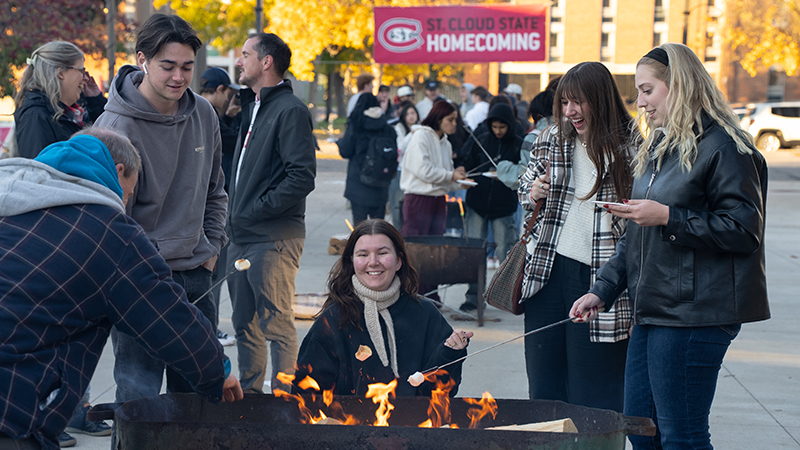 students roast marshmallows around campfire during Homecoming campfire event