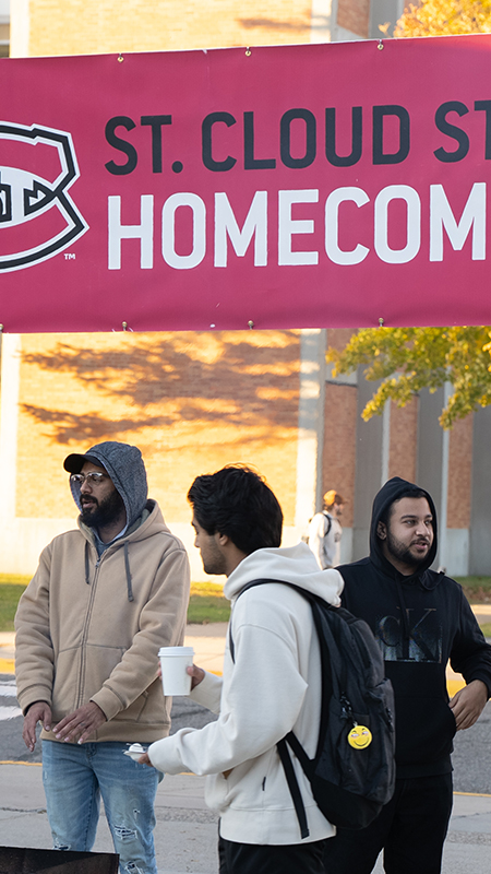 A few SCSU students stand around a fire under a "Homecoming" banner on a fall day