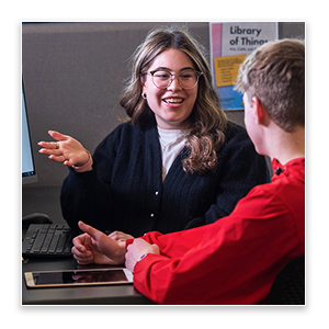 Two people seated at a table discussing information on a laptop, with one person gesturing during the conversation.