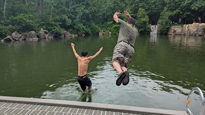 Student and teacher jumping off dock into quarry lake