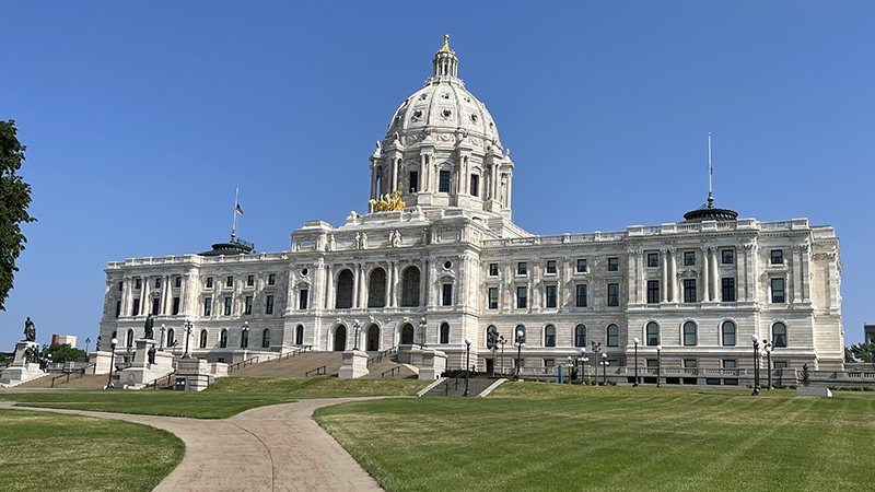 o A wide view of the Minnesota State Capitol building with its white stone façade and domed roof, set against a clear blue sky and green lawn in the foreground.