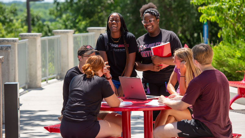 Several students talking and laughing around a red table outside
