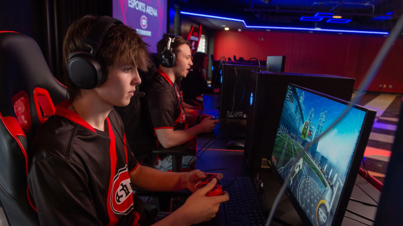 Student wearing headset playing video game on a computer while holding a gaming controller 