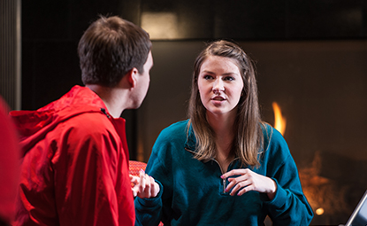 Two people sitting in front of a fireplace talking