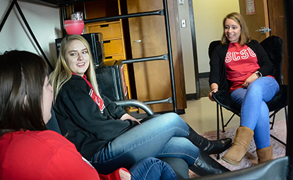 Three women sitting in a residential hall room talking