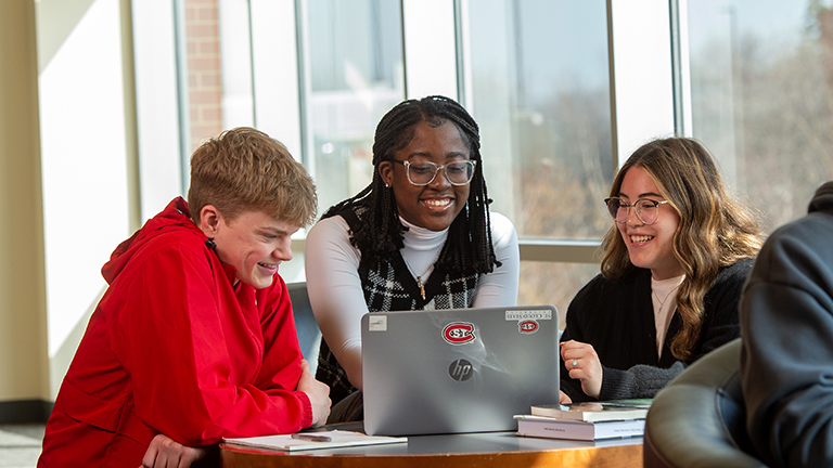 Three new students gather around a laptop at orientation
