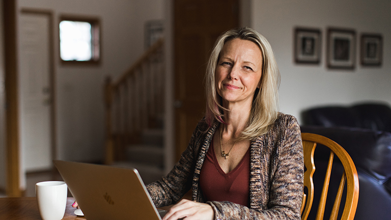 A mom sits at a kitchen table looking at her laptop