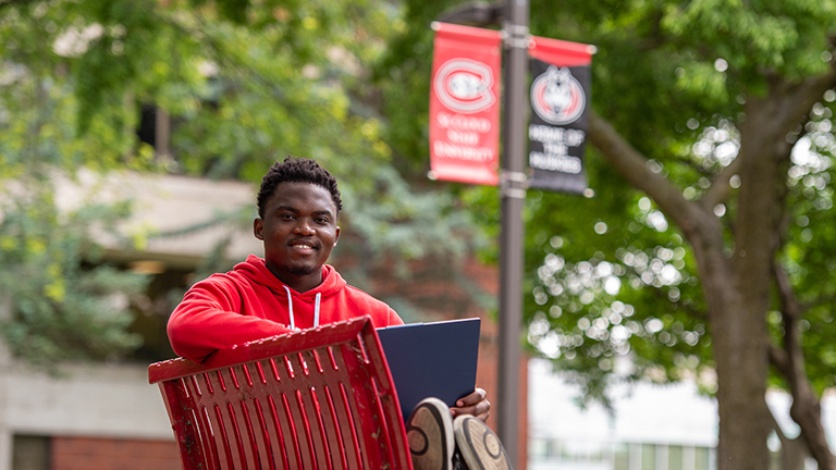 A transfer student sits on a SCSU campus bench with laptop