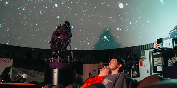Two young men leaning back in their chairs watching a planetarium show