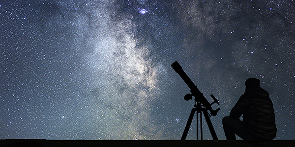 Silhouette of person looking at night sky with telescope