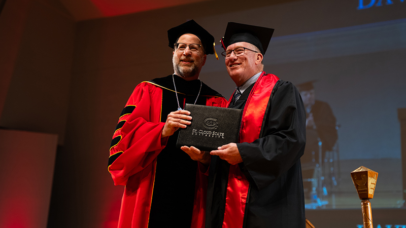 President Tomso poses for a photo with a graduate on the commencement stage